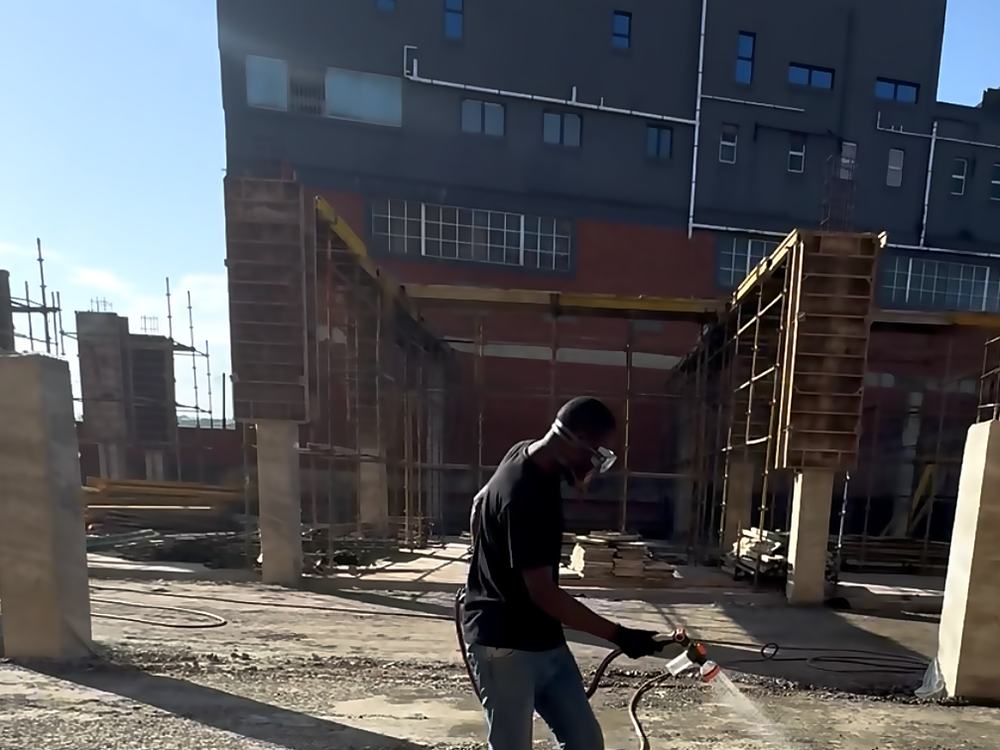 Operator treating prepared ground alongside an existing structure on a commercial site